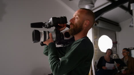 Male-Film-Camera-Operator-Taking-Camera-Off-Tripod-To-Shoot-Handheld-Movie-Or-Video-In-Studio